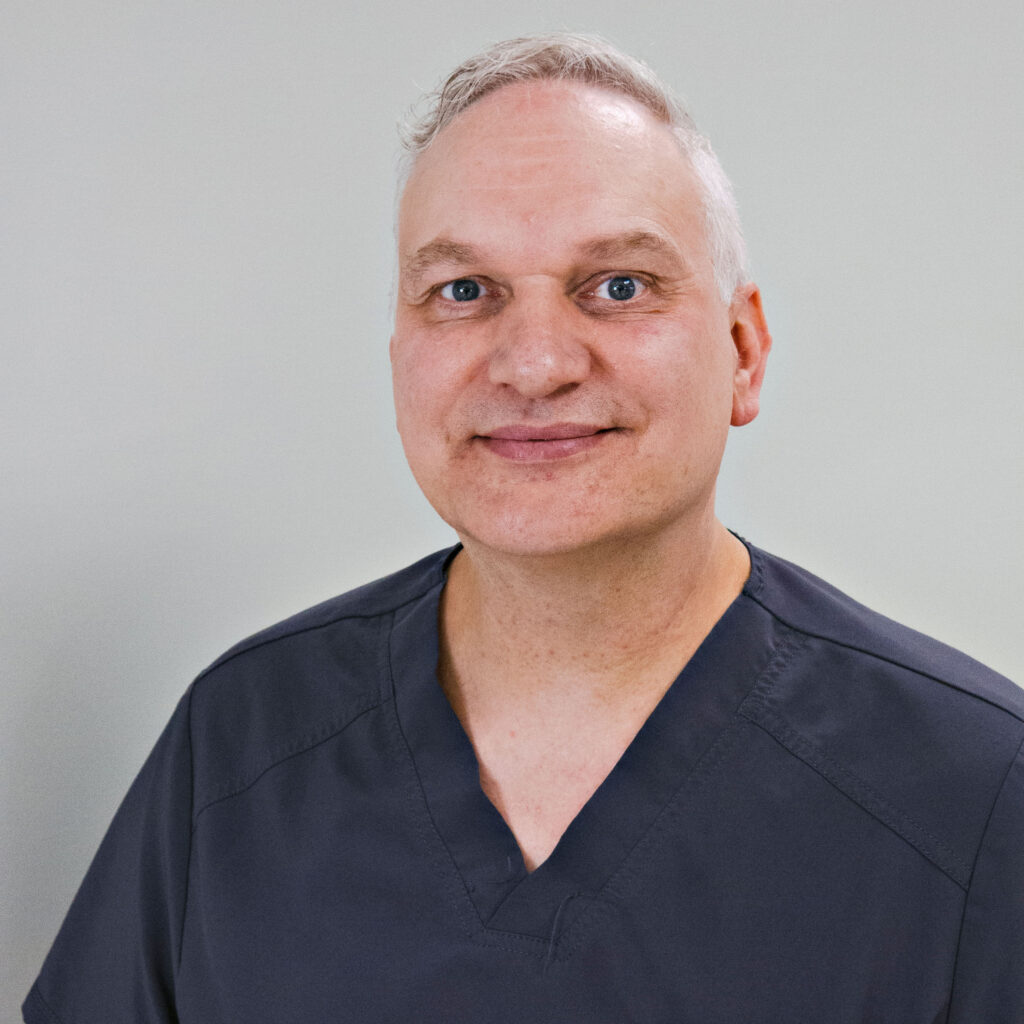 Smiling healthcare professional in grey scrubs against neutral background