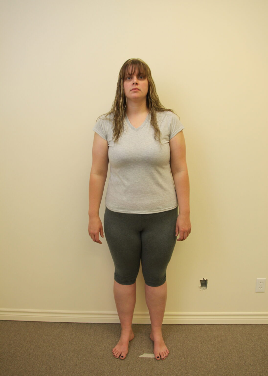 Woman standing against a wall, wearing casual grey clothing