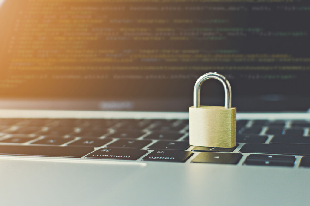 Padlock on laptop keyboard with blurred code on screen