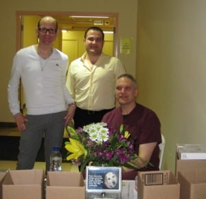Three men at a donation table with flowers and a donation box